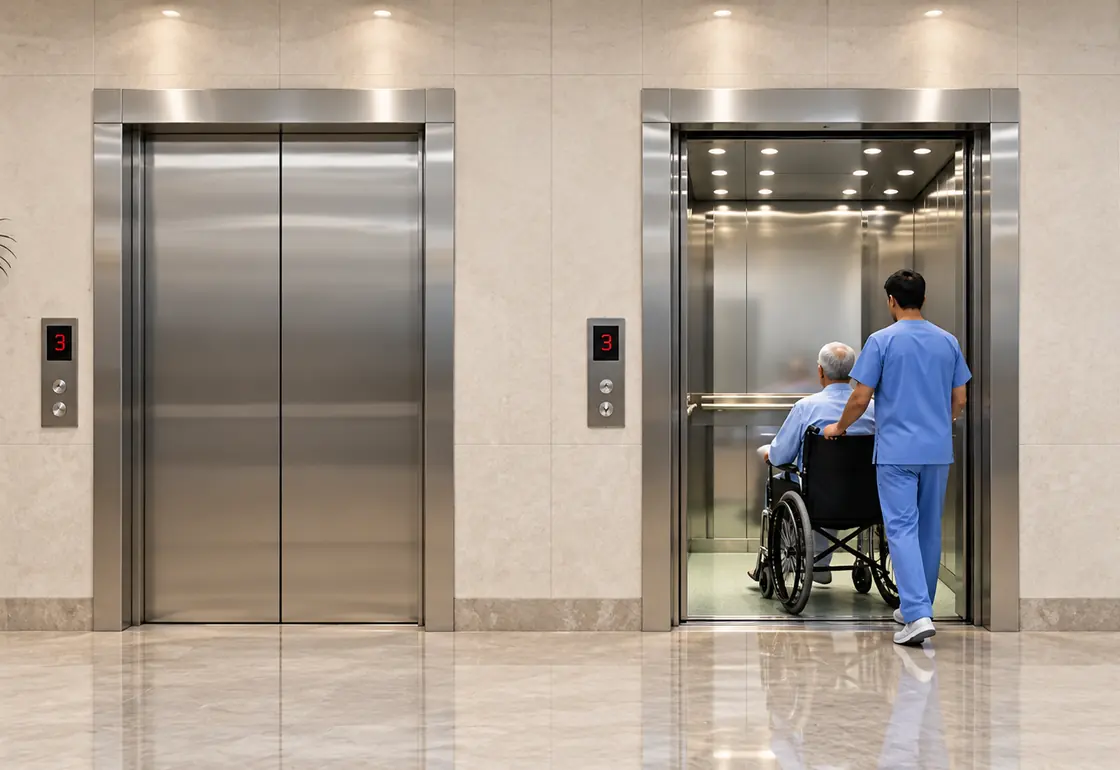 Hospital elevator with a wide stainless-steel cabin, shown with a patient stretcher inside and an attendant wheeling a patient into an adjacent lift